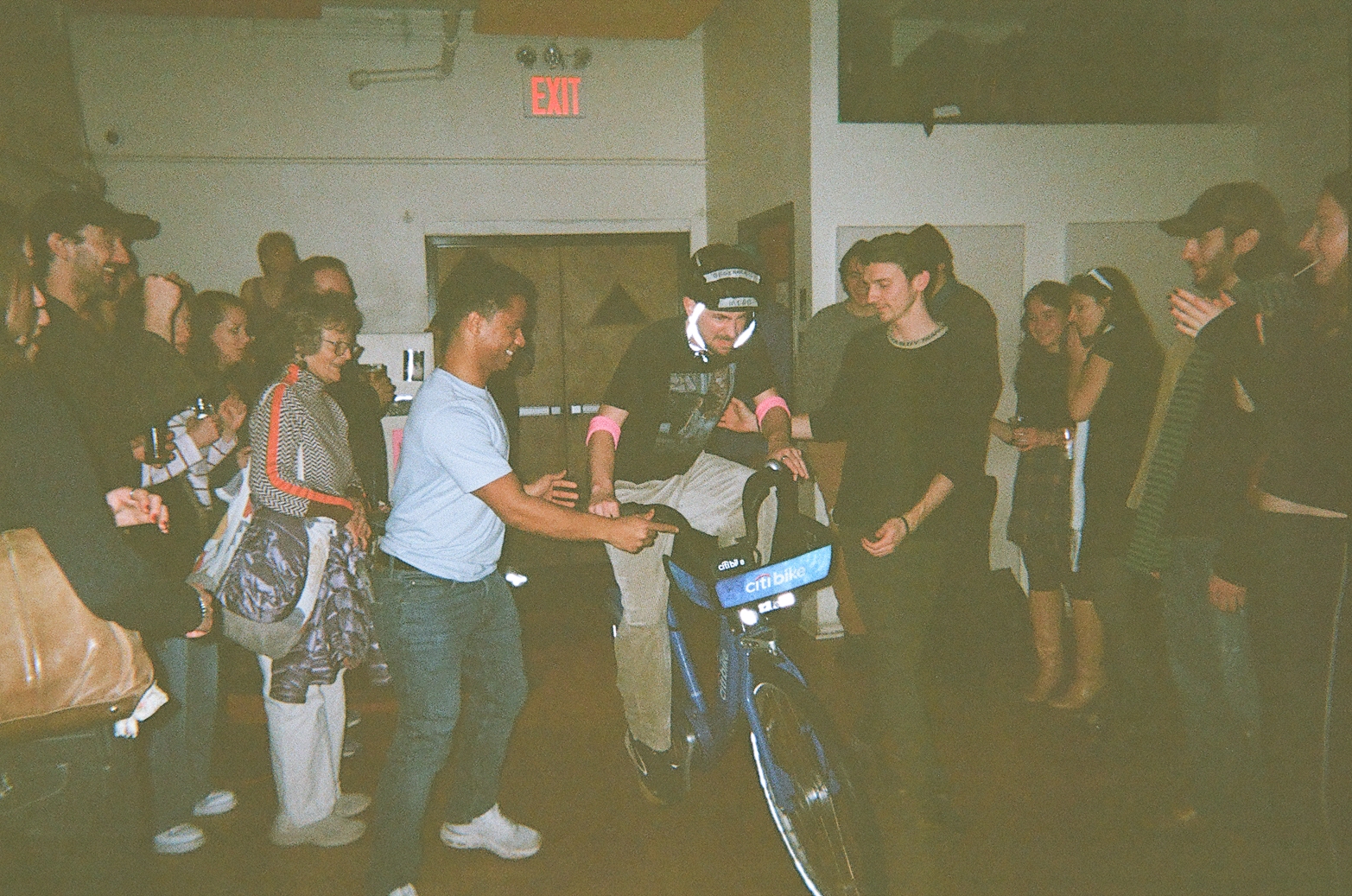 A crowd gathered around a man on a Citi Bike as another man steadies him