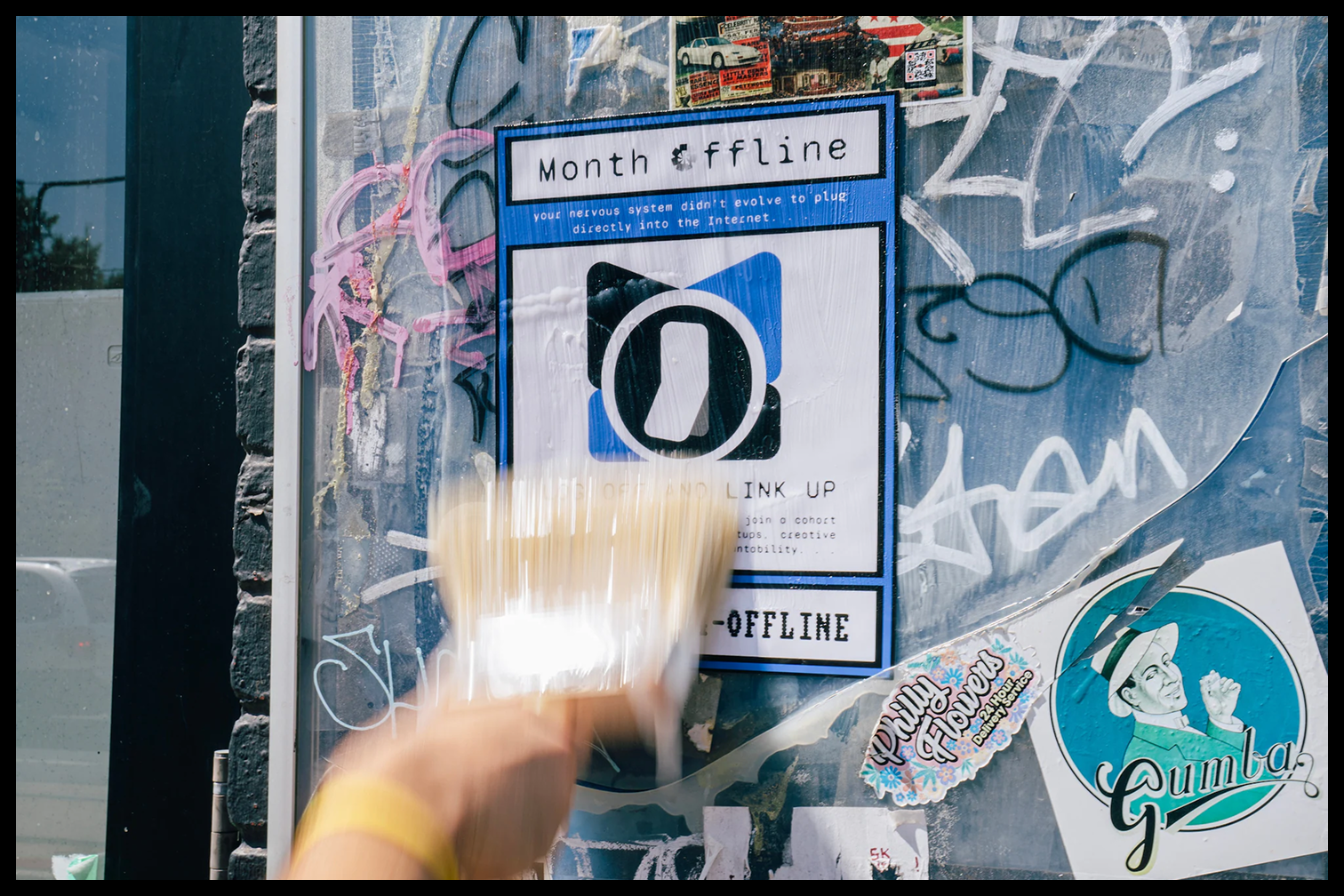 A hand wheat-pasting a Month Offline poster onto a city wall